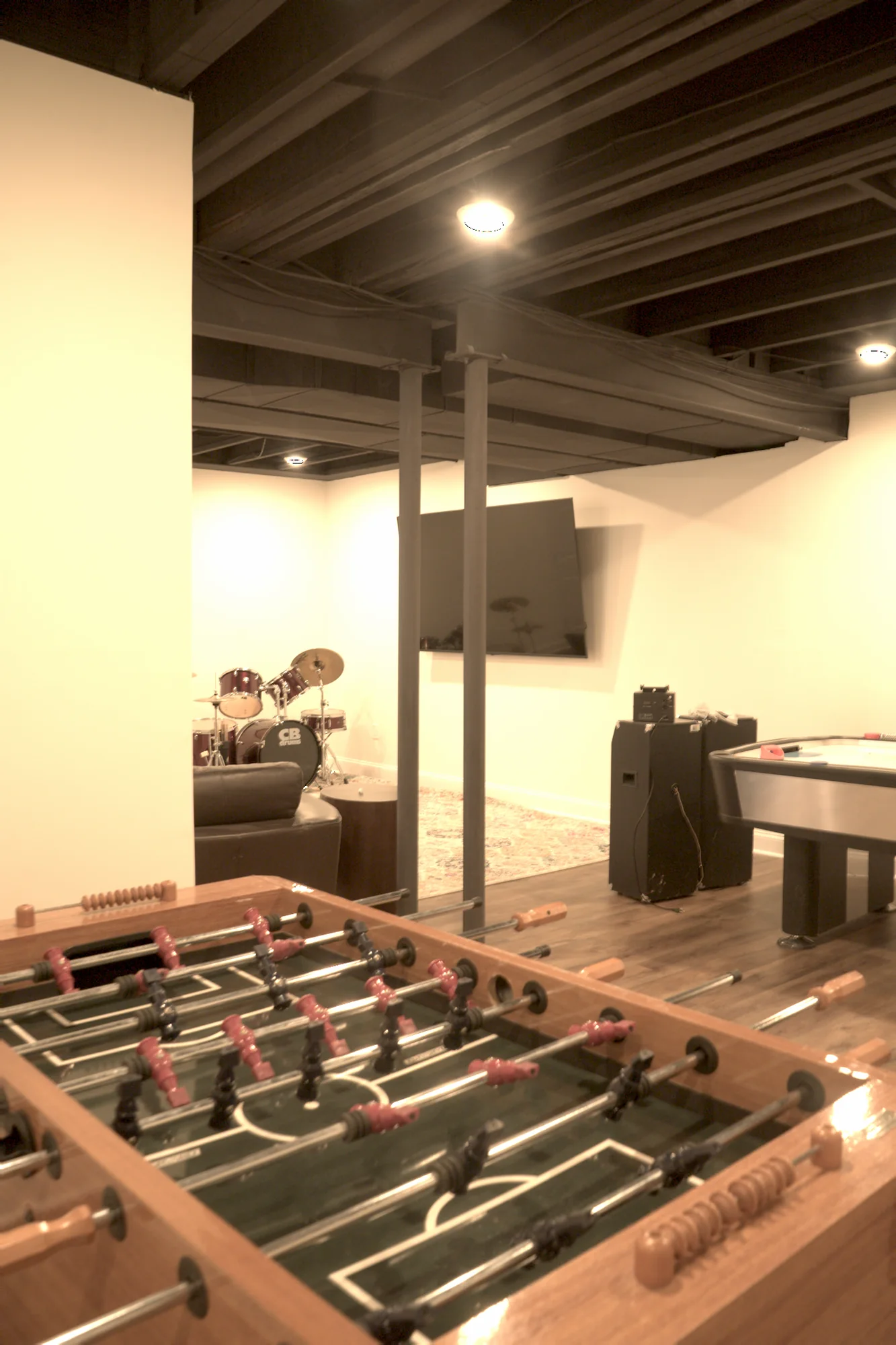 Finished basement game room with foosball table, TV lounge, and black exposed ceiling by Arch Basements.